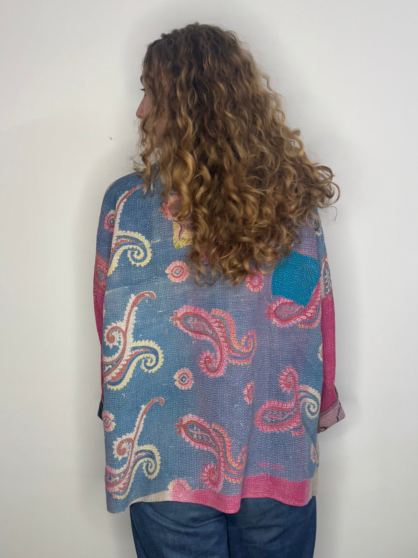 Person wearing a blue patterned jacket against a white wall.