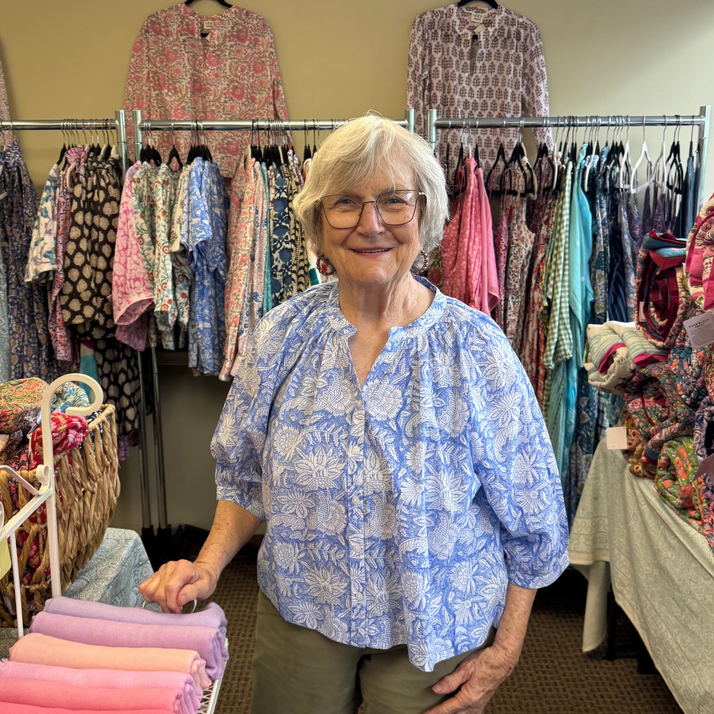 Woman standing in a clothing store surrounded by racks of clothes.
