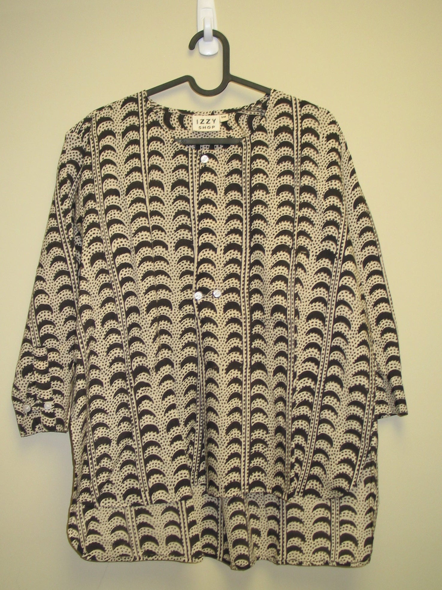 Patterned tunic on a hanger against a beige background. 