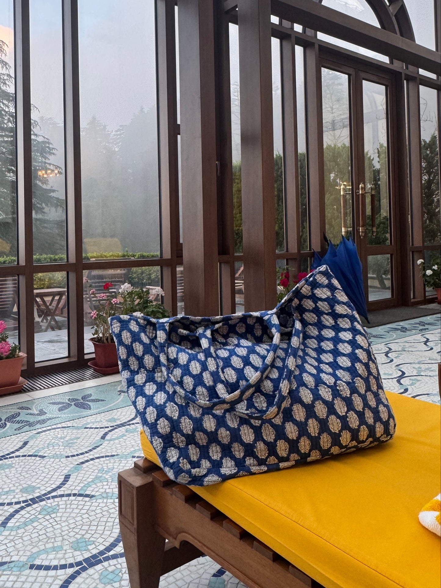 Outdoor patio with glass walls, yellow cushioned chair, and blue patterned bag.