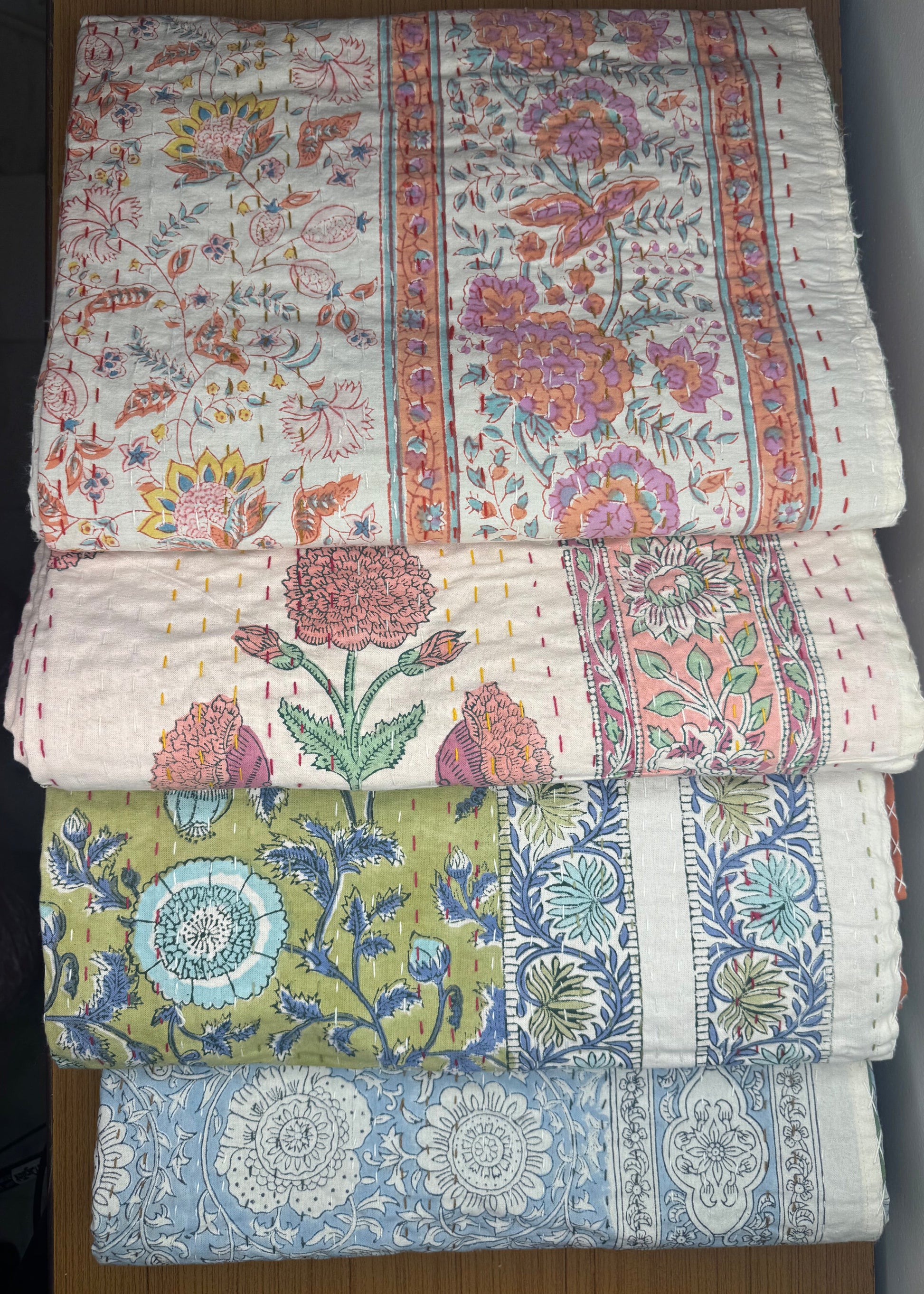 Four floral-patterned quilts stacked on a wooden surface