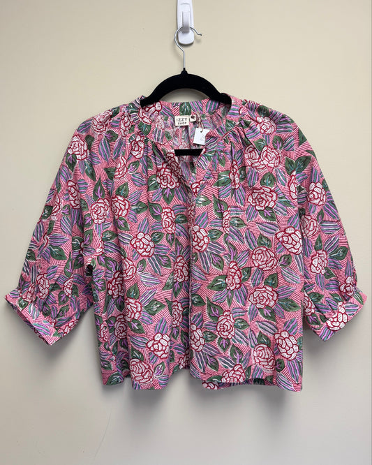 A pink floral blouse with three-quarter sleeves hanging on a black hanger against a plain beige wall.