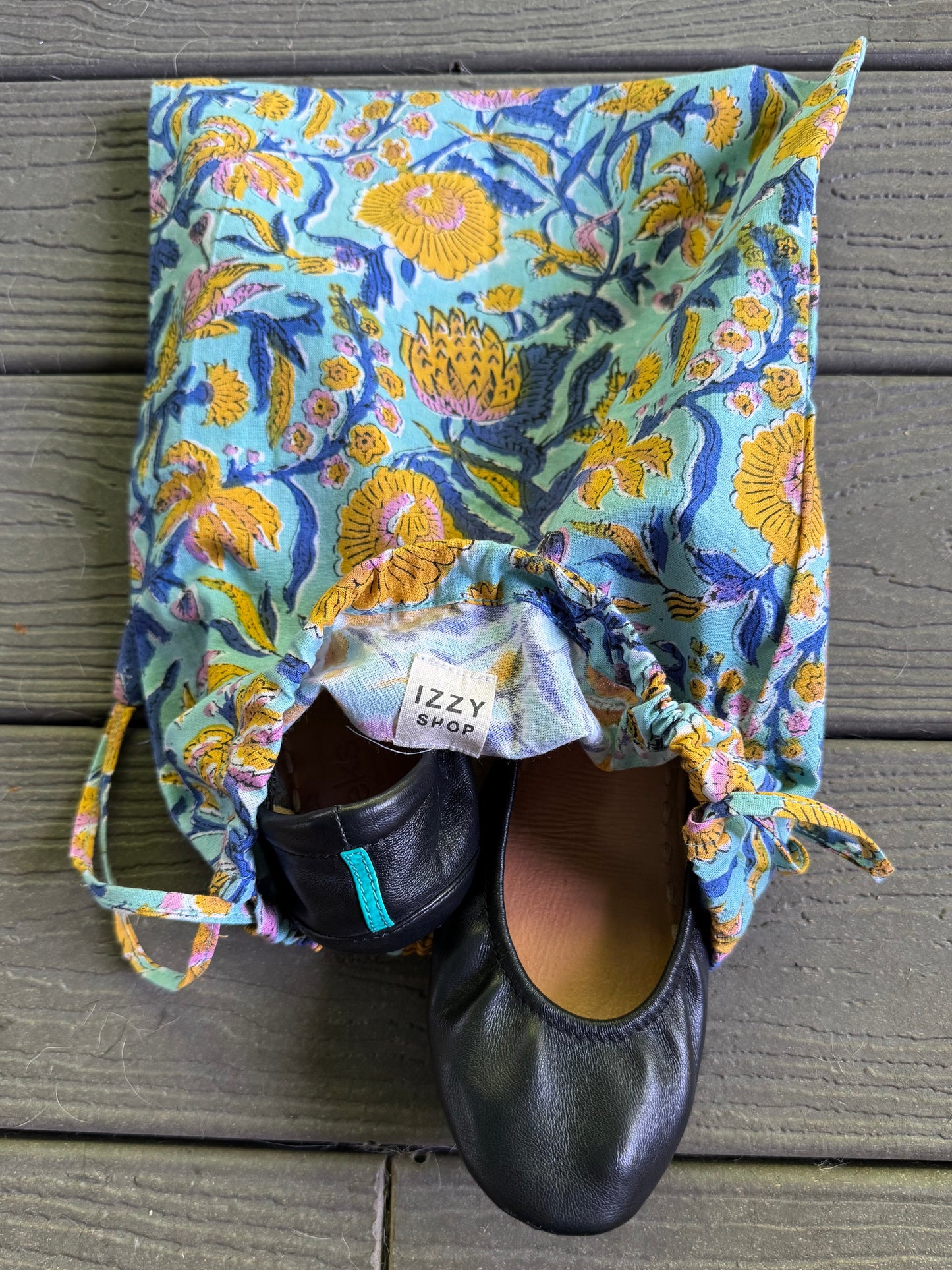 Floral-patterned shoe bag with black shoes inside on a wooden surface