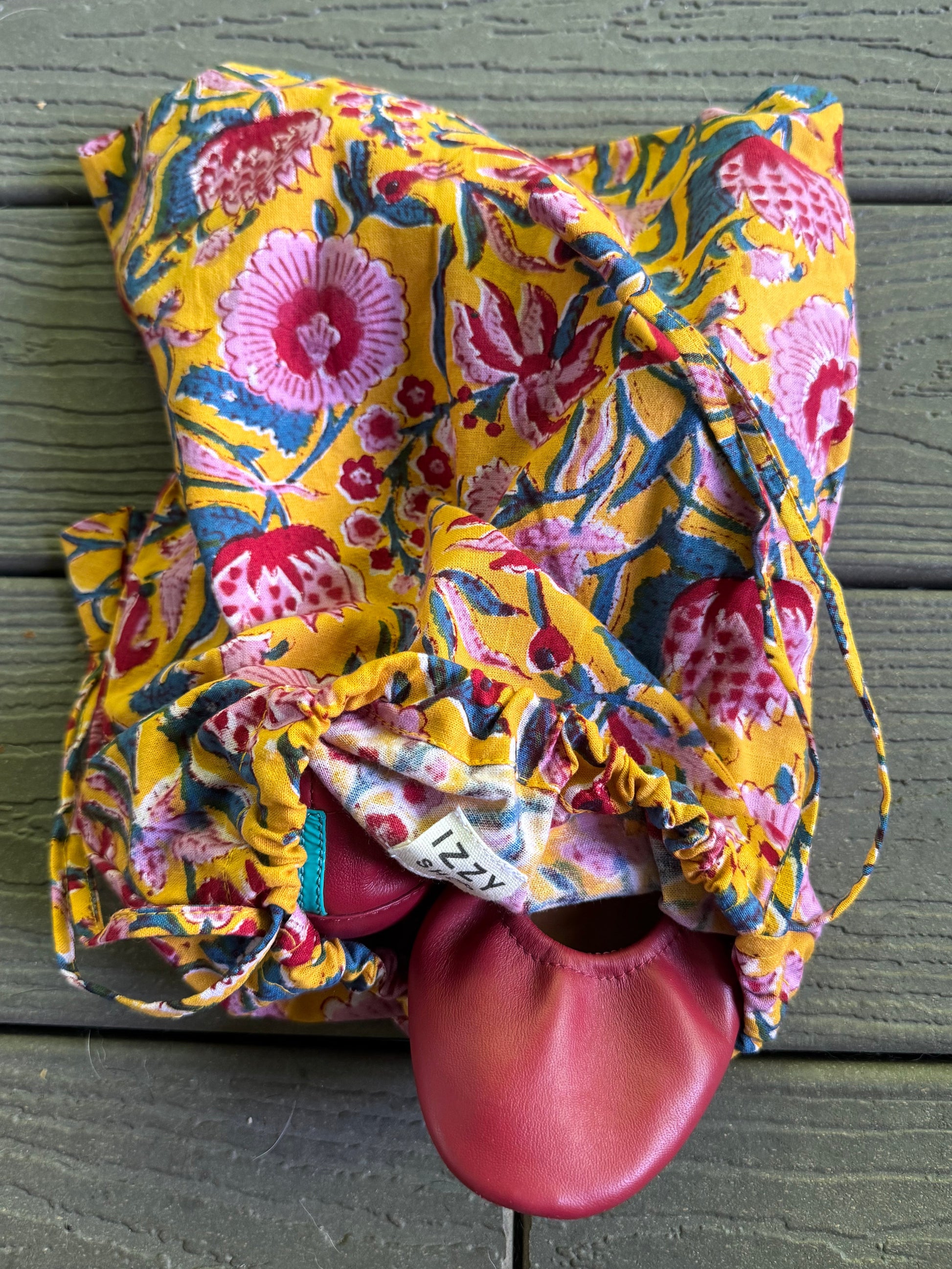 Colorful floral-patterned drawstring bag with a red object inside against a wooden background