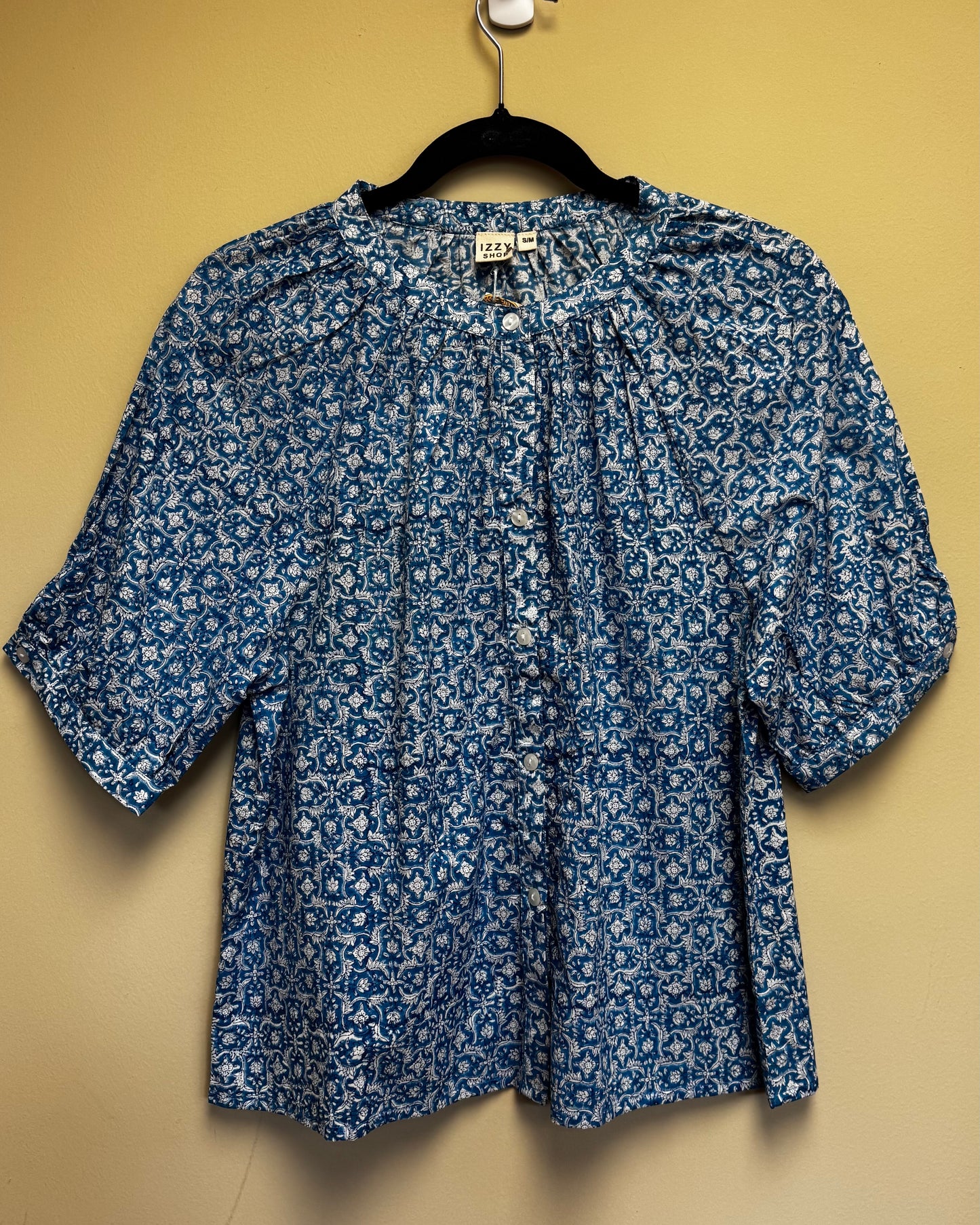 Blue floral patterned blouse on a hanger against a beige background