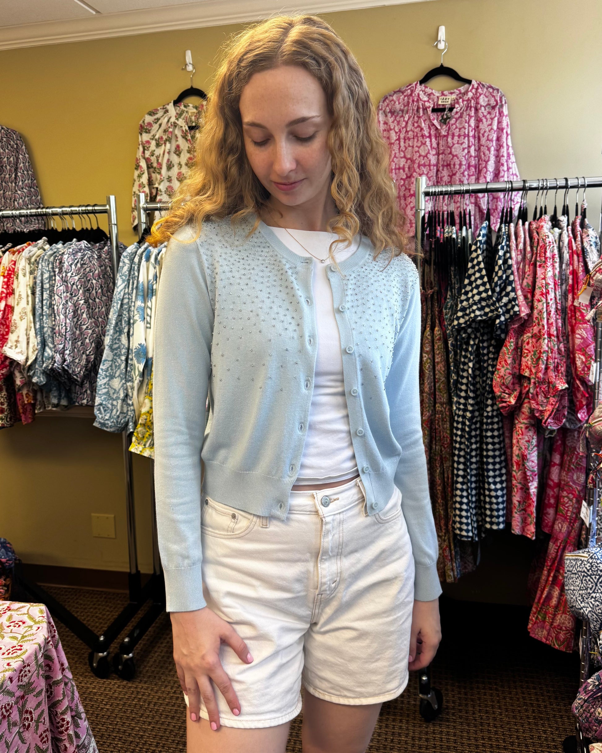 Woman in a clothing store wearing a light blue cardigan and white shorts.