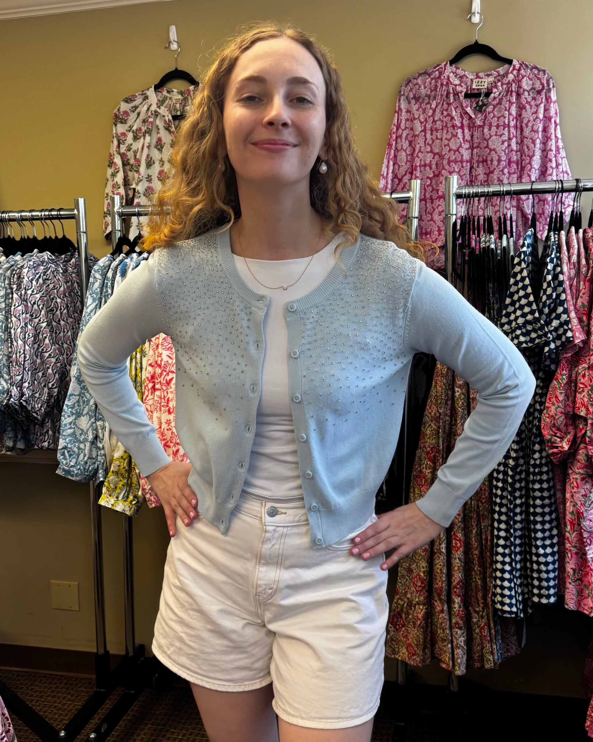 Woman standing in a clothing store with racks of patterned shirts behind her