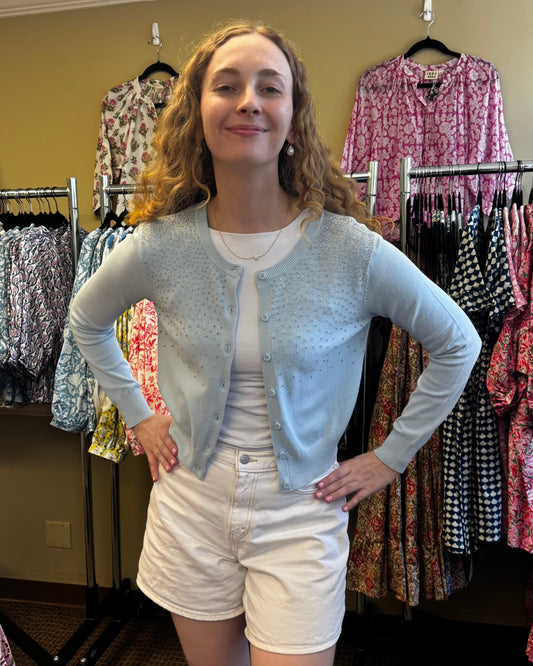 Woman standing in a clothing store with racks of patterned shirts behind her