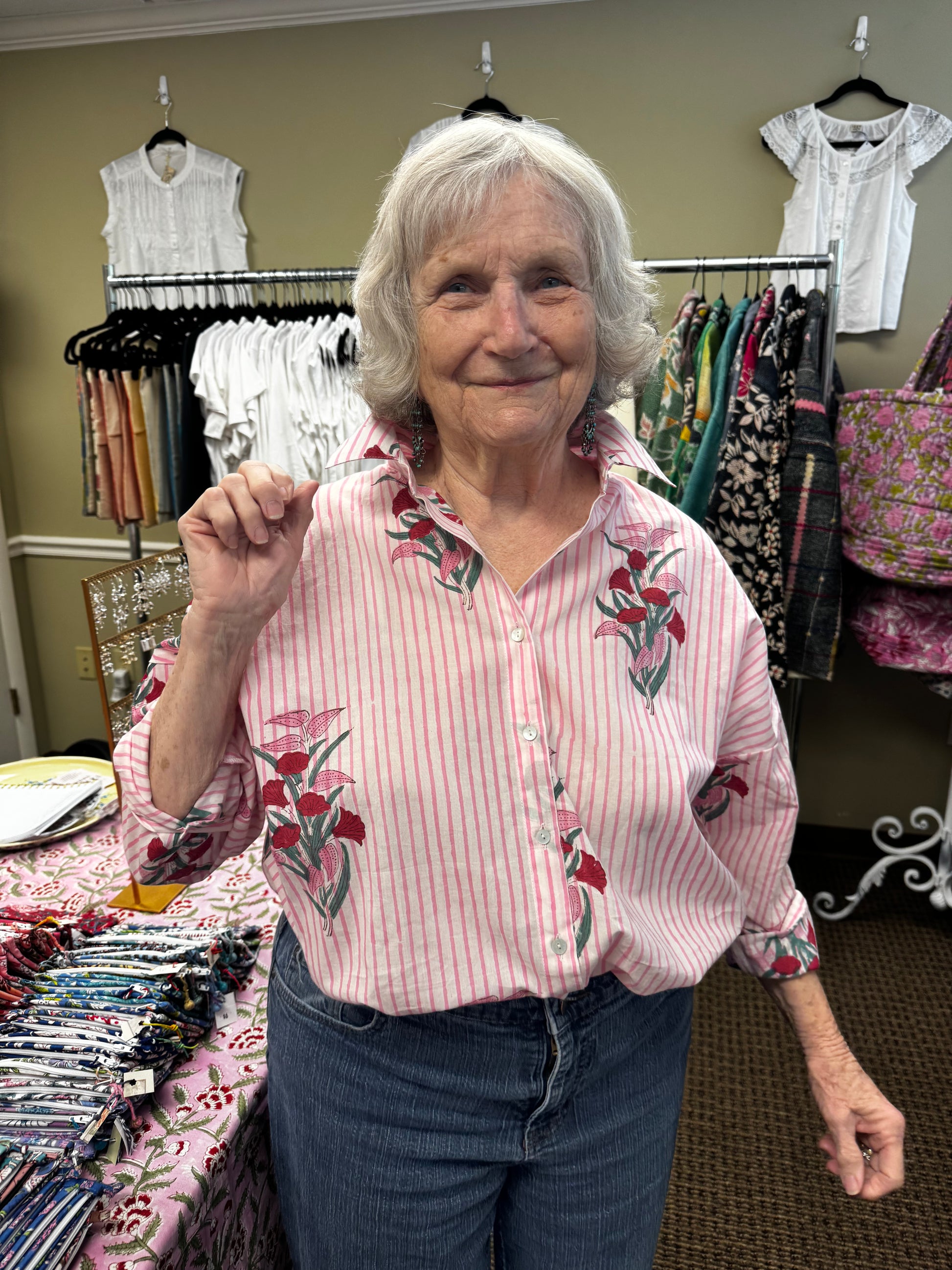 Woman wearing a pink floral blouse standing in front of a rack of clothes.
