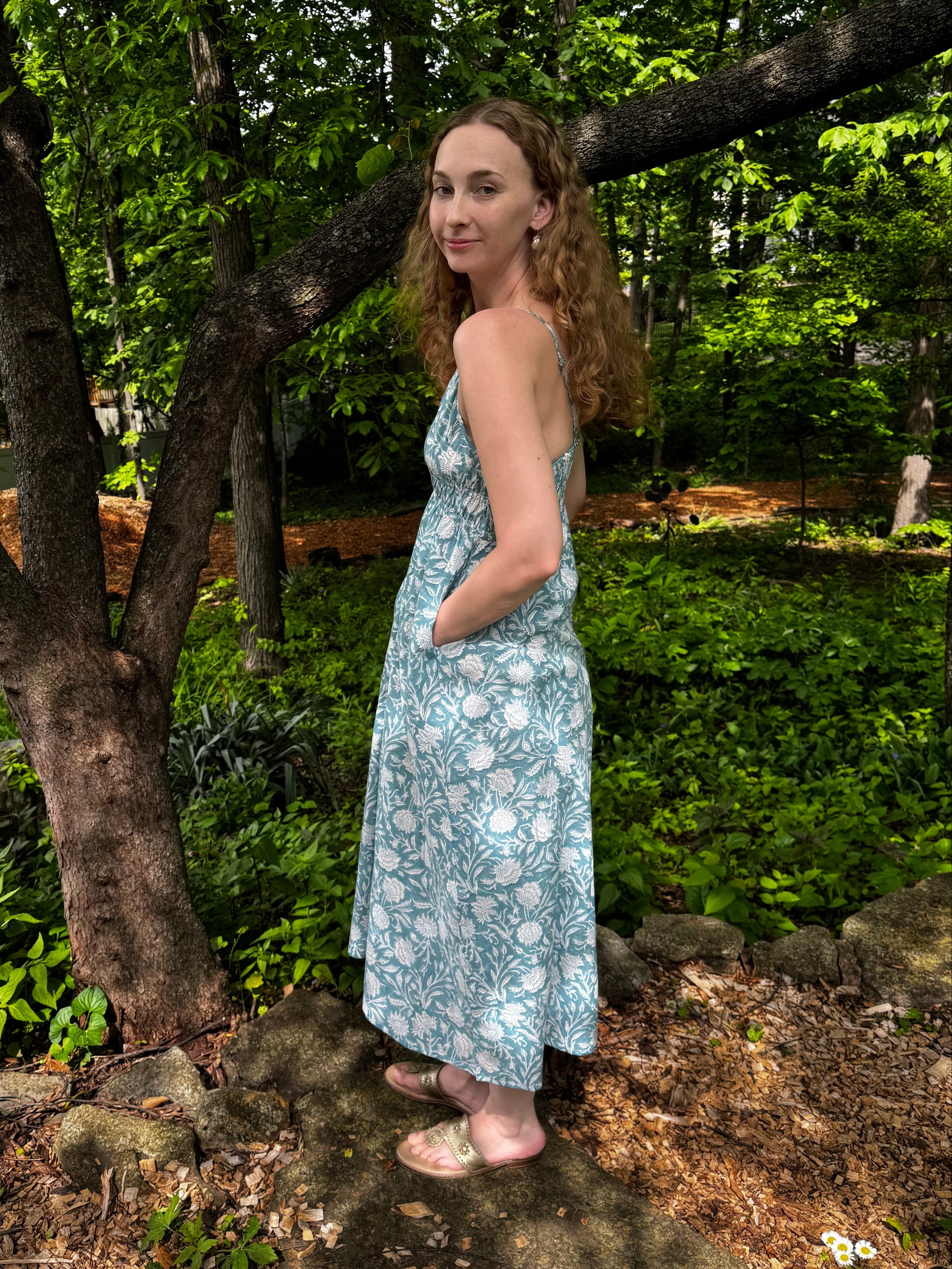 Person in a patterned dress standing among trees and rocks