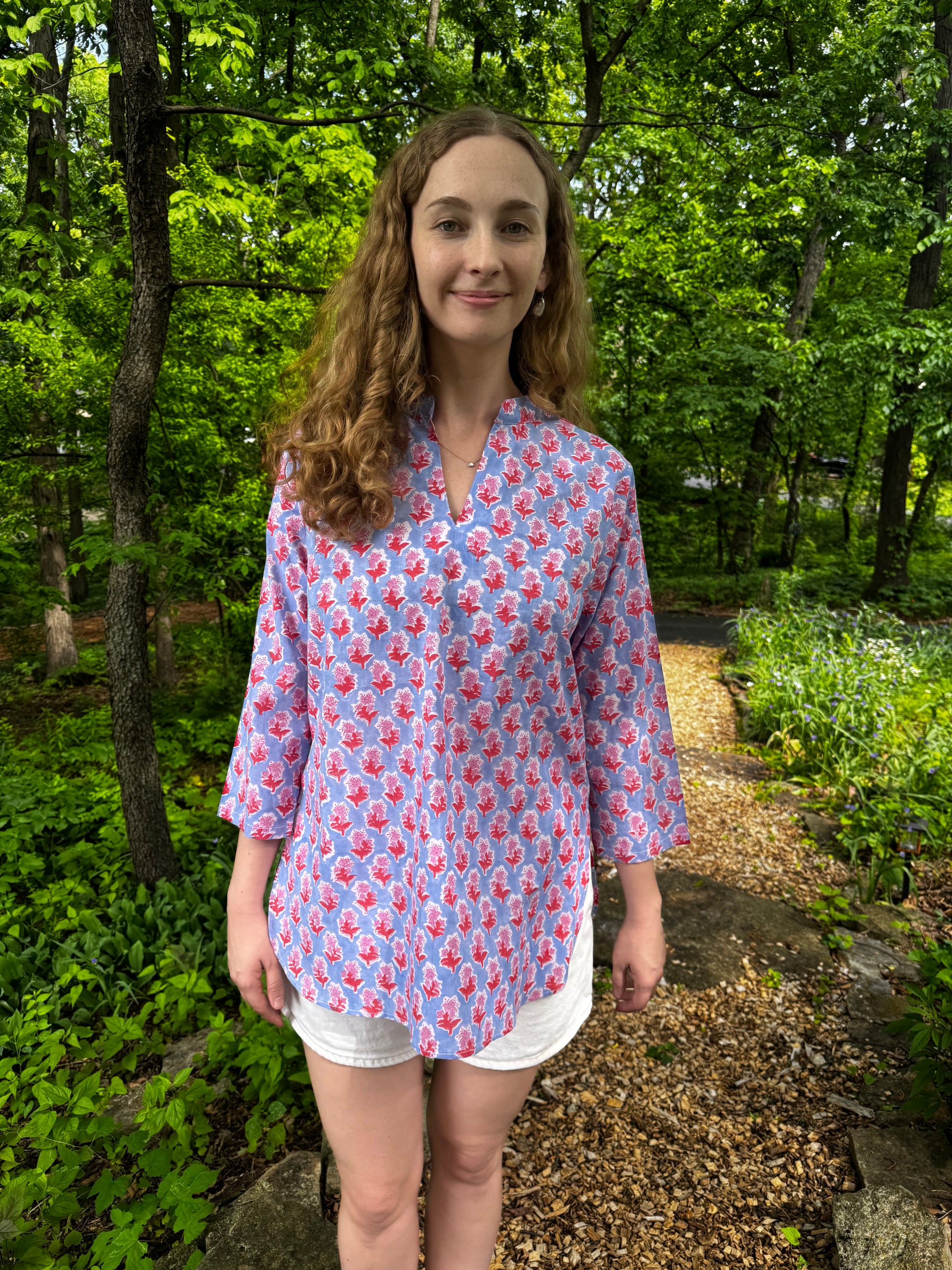 Woman wearing a pink floral blouse standing in a forested area