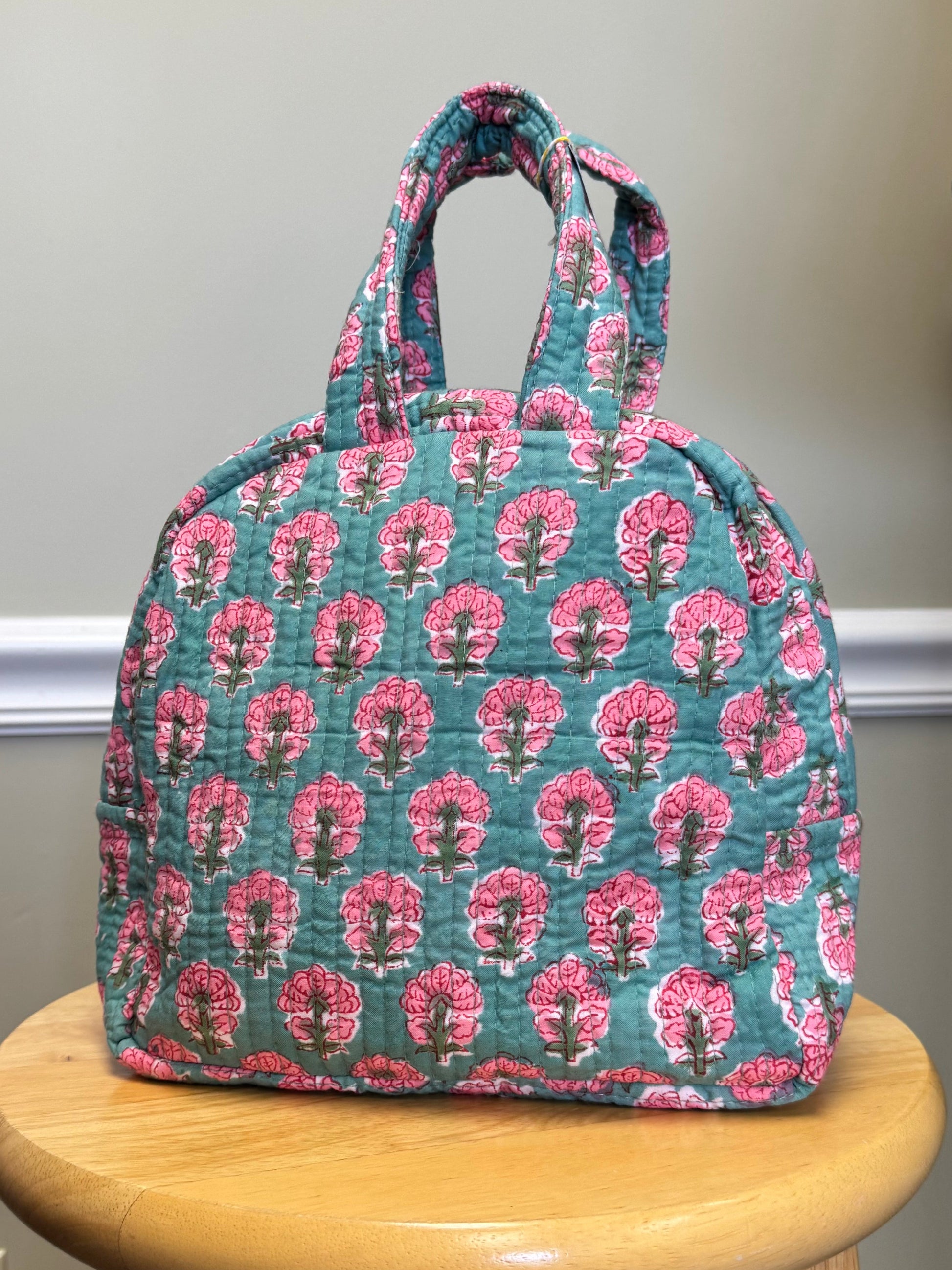 Floral-patterned bag on a wooden stool against a neutral wall.