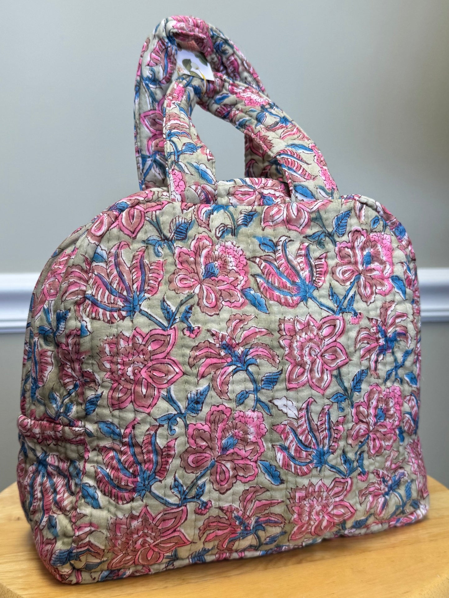Floral-patterned bag on a wooden chair against a neutral wall.
