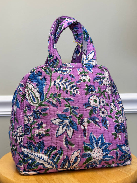 Floral-patterned purple bag on a wooden stool against a neutral wall.